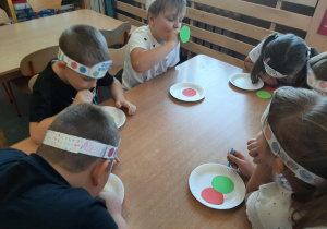 Dzieci siedzą przy stoliku. Zabawa polega na przenoszeniu papierowej kropki za pomocą słomki.