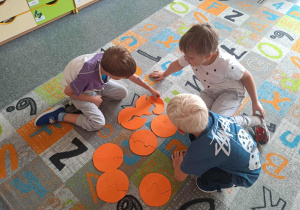 Dzieci siedzą na dywanie i dobierają dwie połówki kropek tak aby pasowały do siebie jak puzzle.