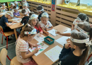 Dzieci siedzą przy stoliku i rysują kropki na kartce.