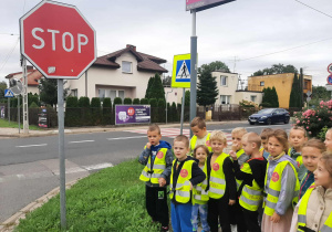 Dzieci stoją na chodniku przy znaku drogowym stop.
