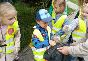 Dzieci zbierają papierki z trawnika.