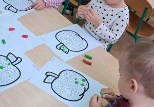 Dzieci przy stoliku wylepiają plasteliną kontur jabłka