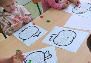 Dzieci przy stoliku wylepiają plasteliną kontur jabłka