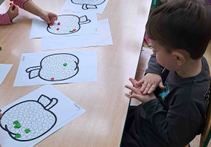 Dzieci przy stoliku wylepiają plasteliną kontur jabłka