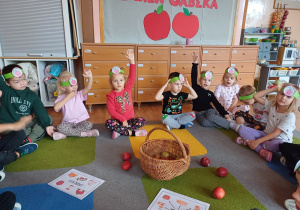 Dzieci siedzą na dywanie podczas obchodów "Dnia Jabłka"
