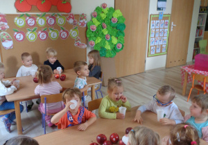 Dzieci degustują przy stole sok jabłkowy i jabłka.