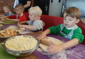 Dzieci przy stole wałkują ciasto na pizzę.