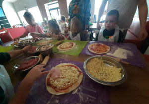 Dzieci przy stole przygotowują pizzę.