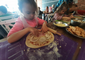 Dzieci przy stole przygotowują pizzę.