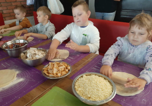 Dzieci przy stole przygotowują pizzę.