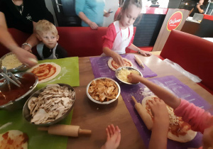 Dzieci przy stole przygotowują pizzę.
