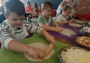 Dzieci przy stole przygotowują pizzę.