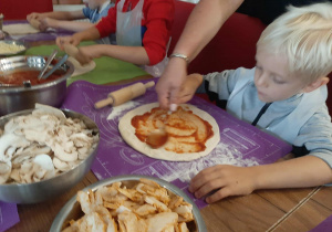Dzieci przy stole przygotowują pizzę.