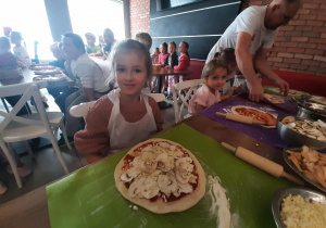 Dzieci przy stole przygotowują pizzę.