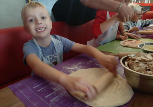 Dzieci przy stole przygotowują pizzę.