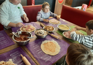 Dzieci przy stole przygotowują pizzę.