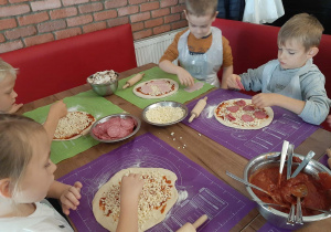 Dzieci przy stole przygotowują pizzę.