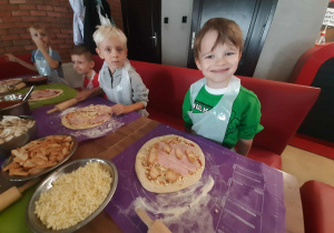 Dzieci przy stole przygotowują pizzę.