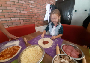 Dzieci przy stole przygotowują pizzę.