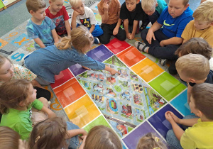 Dzieci oglądają planszę z makietą ruchu ulicznego w mieście i wskazują miejsca, w których powinny stać określone znaki drogowe