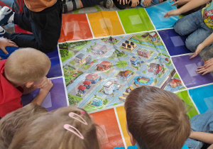 Dzieci oglądają planszę z makietą ruchu ulicznego w mieście i wskazują miejsca, w których powinny stać określone znaki drogowe