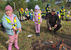 Dzieci pieką kiełbaski nad ogniskiem pod opieką pana leśnika