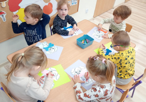Dzieci przy stoliczkach tworzą swojego pieska na papierze.