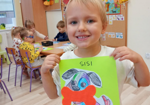 Lilka zadowolona prezentuje swoją pracę plastyczną.