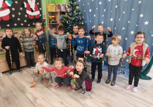 Przy dekoracji świątecznej dzieci pozują do zdjęcia. W ręku trzymają swój wykonany łańcuch choinkowy.