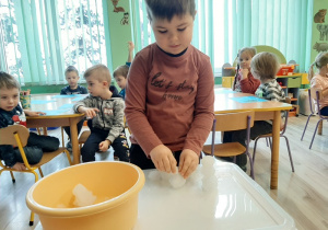 Chłopiec stoi przy małym stoliku i składa bałwana ze zrobionych kul.