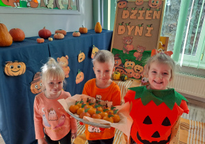 Trójka dzieci z grupy „Pszczółki” częstuje pomarańczą