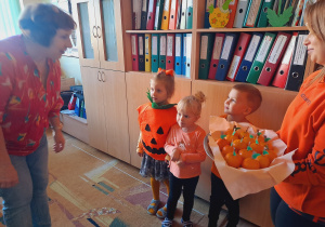 Trójka dzieci z grupy „Pszczółki” częstuje pomarańczą