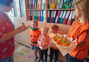 Trójka dzieci z grupy „Pszczółki” częstuje pomarańczą