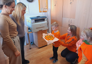 Trójka dzieci z grupy „Pszczółki” częstuje pomarańczą