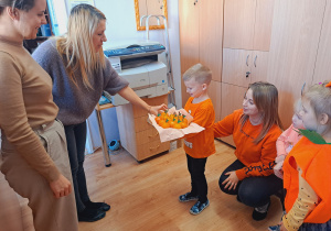 Trójka dzieci z grupy „Pszczółki” częstuje pomarańczą