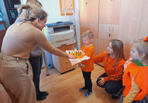 Trójka dzieci z grupy „Pszczółki” częstuje pomarańczą