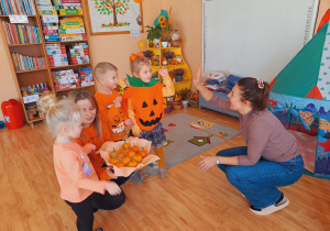 Trójka dzieci z grupy „Pszczółki” częstuje pomarańczą