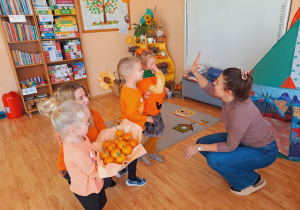 Trójka dzieci z grupy „Pszczółki” częstuje pomarańczą