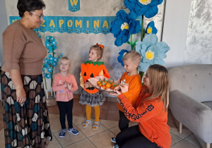 Trójka dzieci z grupy „Pszczółki” częstuje pomarańczą