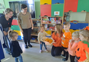 Trójka dzieci z grupy „Pszczółki” częstuje pomarańczą