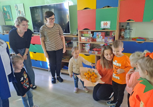 Trójka dzieci z grupy „Pszczółki” częstuje pomarańczą