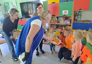 Trójka dzieci z grupy „Pszczółki” częstuje pomarańczą