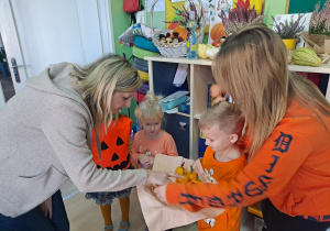 Trójka dzieci z grupy „Pszczółki” częstuje pomarańczą