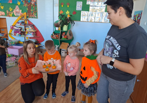 Trójka dzieci z grupy „Pszczółki” częstuje pomarańczą