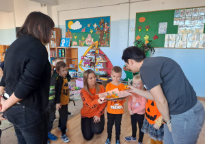 Trójka dzieci z grupy „Pszczółki” częstuje pomarańczą