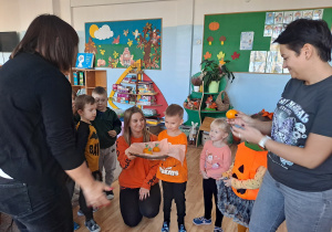 Trójka dzieci z grupy „Pszczółki” częstuje pomarańczą