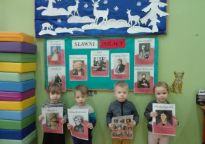 Dzieci stoją przy tablicy trzymając przed sobą obrazki przedstawiające sylwety sławnych Polaków