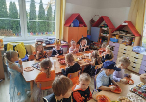 Dzieci siedzą przy stołach i zjadają słodki poczęstunek.