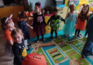 Dzieci w przebraniach tańczą na dywanie trzymając się za ręce.