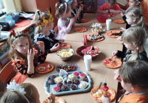 Dzieci siedzą przy stole i próbują różnorodnych słodyczy.